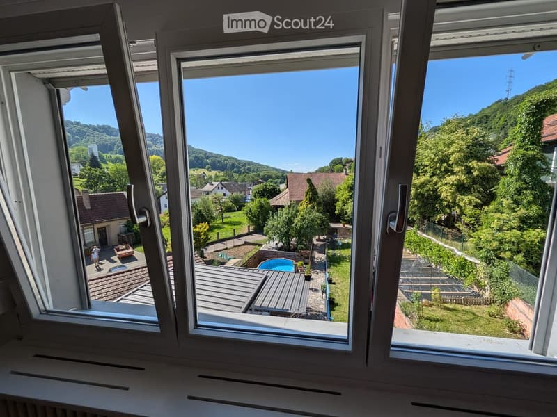 View from a balcony showing a scenic landscape with houses, trees, and a swimming pool in the foreground.