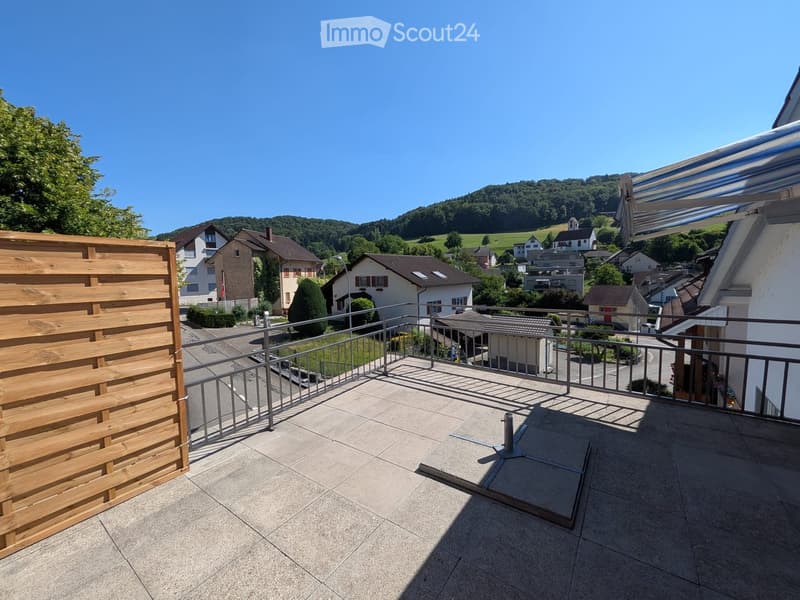 Balcony with tiled floor, metal railing, wooden privacy screen, and scenic view of a town and hills.