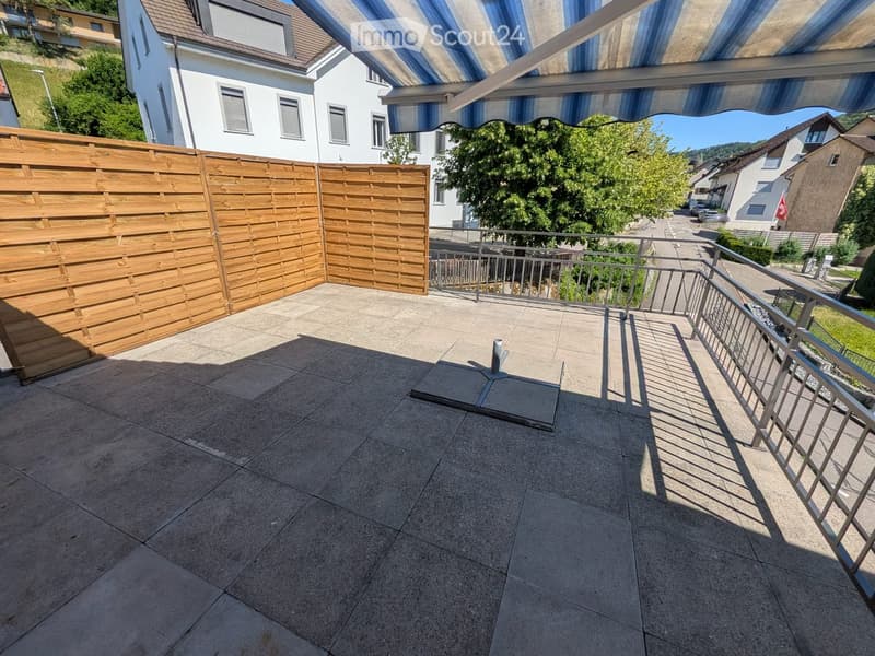 Balcony with tiled floor, wooden fence, metal railing, and striped awning.