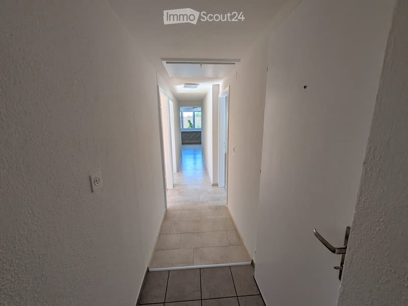 Empty hallway with tiled floor, white walls, and a door at the end leading to another room.