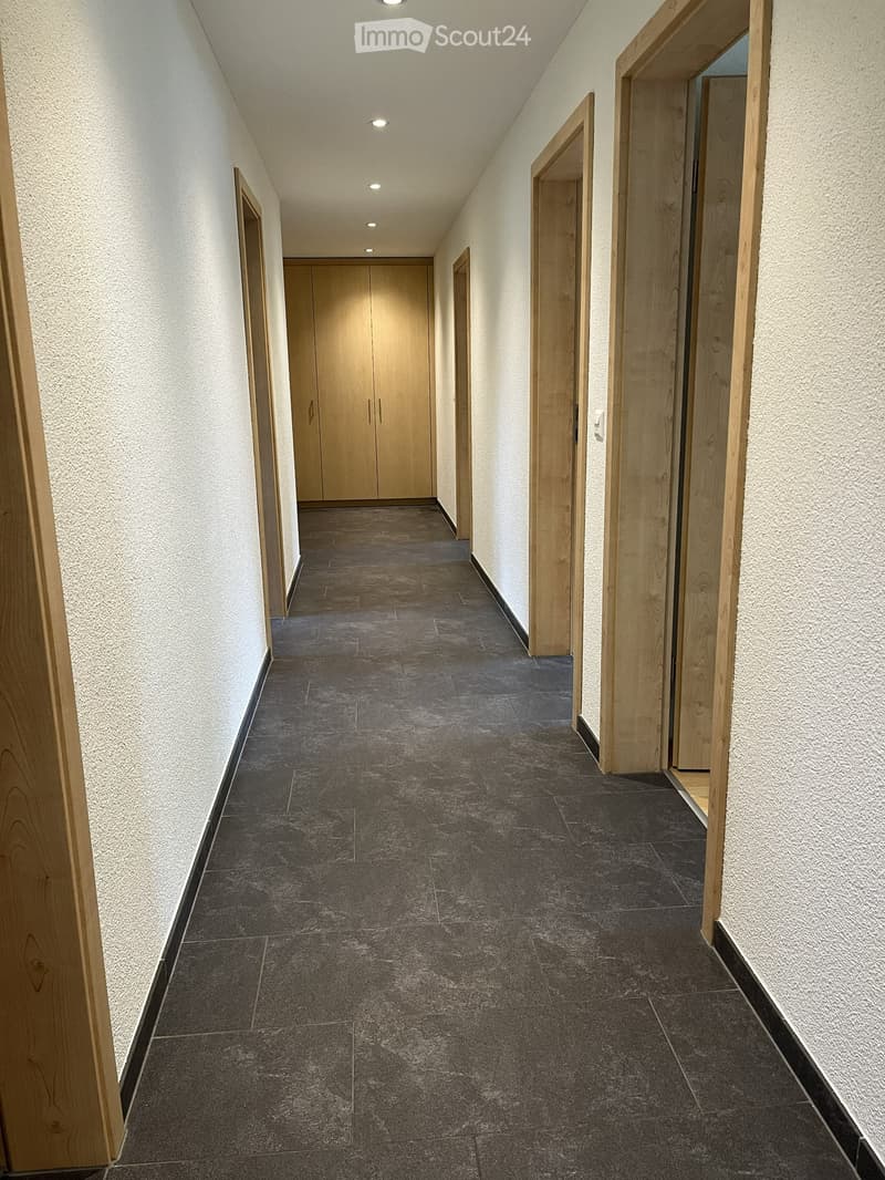 Clean, modern hallway with dark tiled flooring, light-colored walls, and wooden doors on both sides.