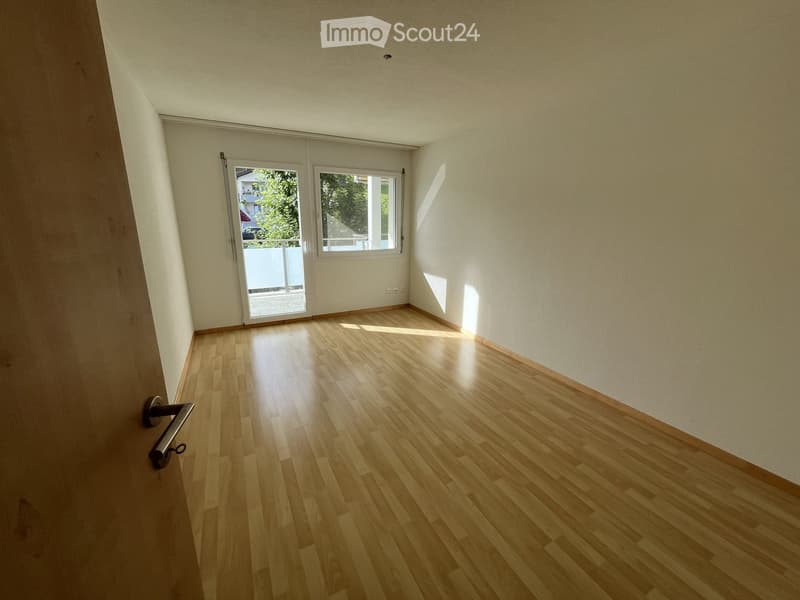 Empty room with wooden flooring, white walls, and a sliding glass door leading to a balcony.