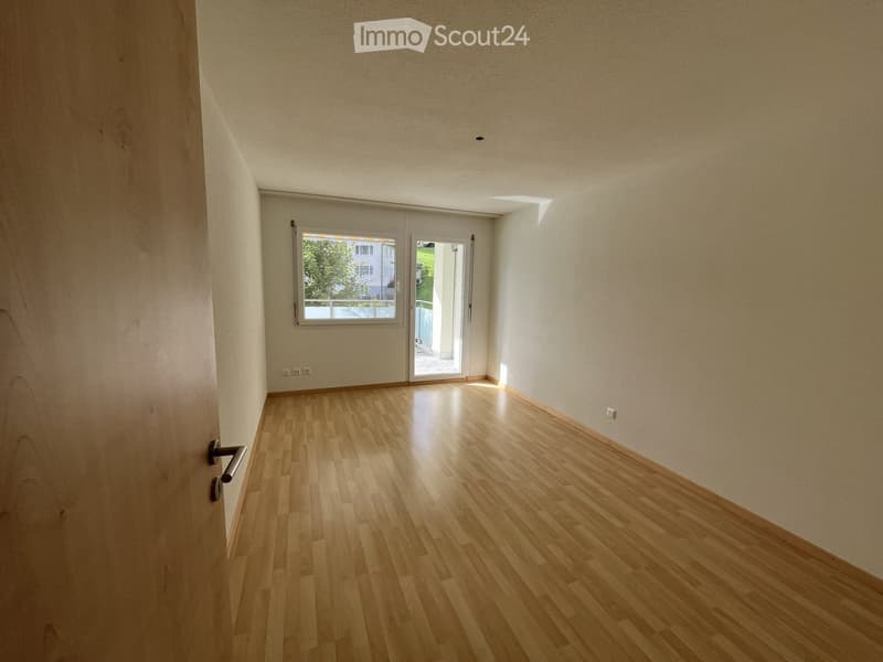 Empty room with light wooden flooring, white walls, and large windows and sliding doors leading to an outdoor area.