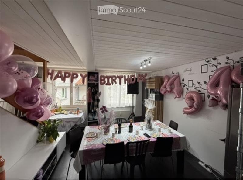 A decorated dining area with a table set for a celebration, featuring balloons, a screen, and floral arrangements.