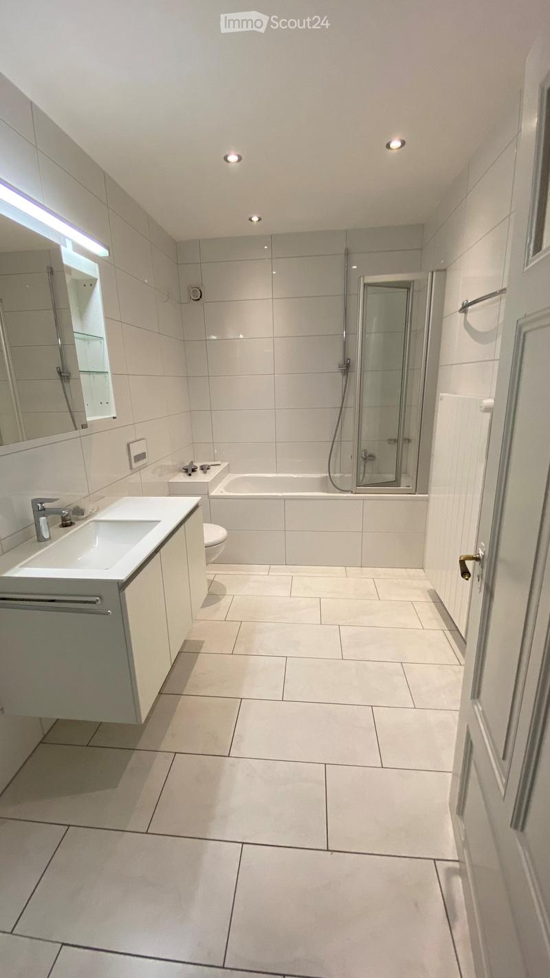modern bathroom with white tiles, bathtub, shower, toilet, sink, mirror, and radiator