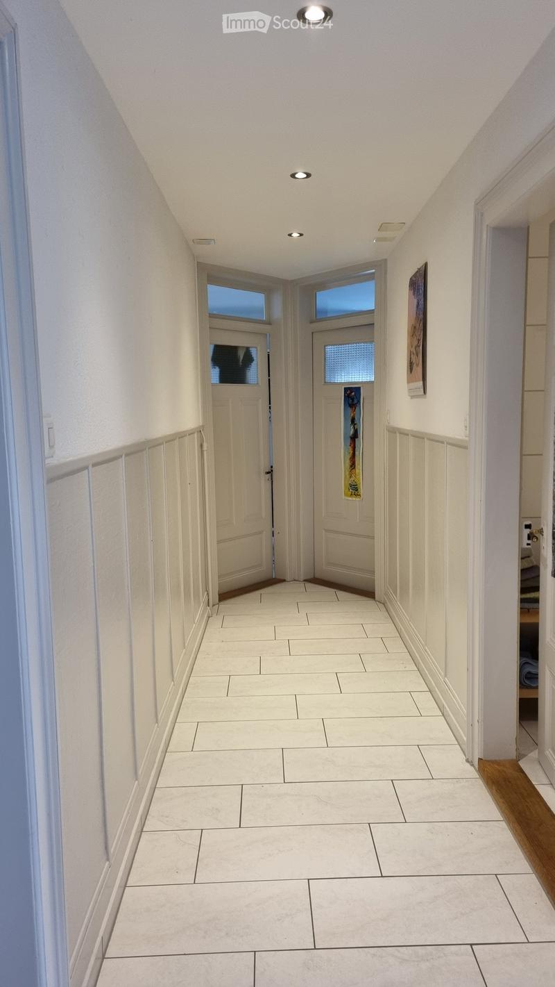 White tiled floor, white walls, two doors, ceiling lights, paintings on the wall