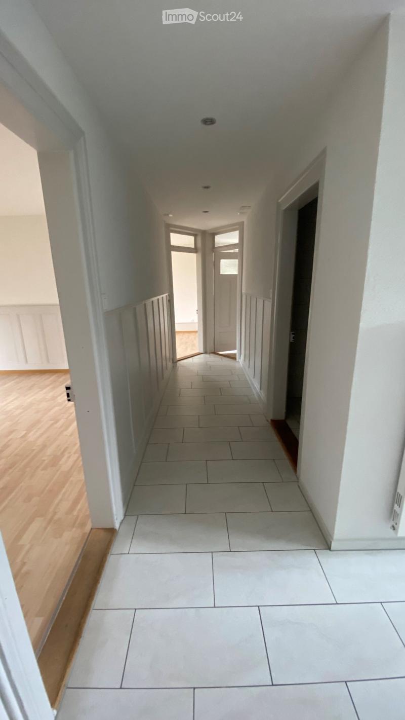 Empty hallway with white tiles, wooden floor, white walls, white doors, ceiling lights