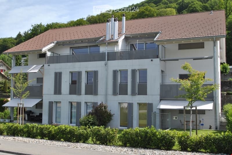 Modern two-story house with white facade, large windows, multiple balconies, and a well-maintained garden.