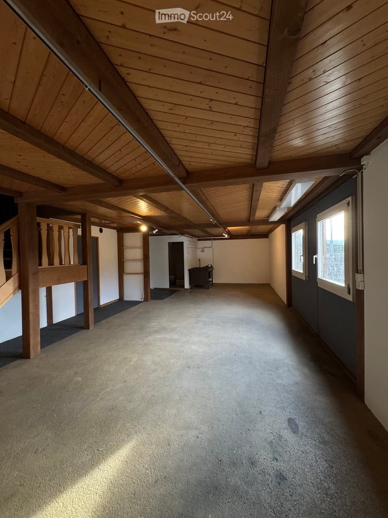 Empty attic space with wooden beams, exposed ceiling, carpeted floor, and small windows on one side.