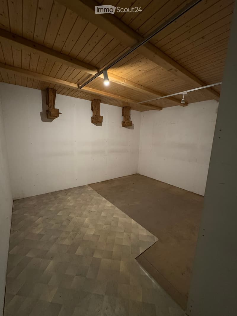 Empty attic space with exposed wooden beams and a slanted wooden ceiling. The floor is made of wooden planks, and the walls are white.