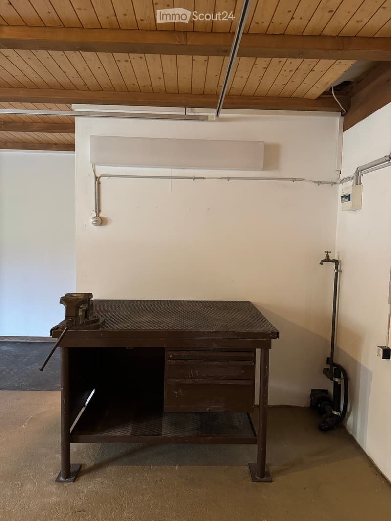 Empty room with a workbench, exposed pipes, and a wooden ceiling.