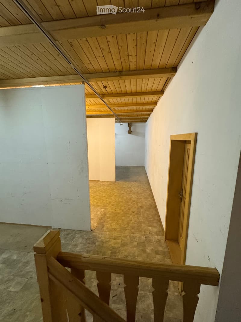 Wooden staircase with a simple wooden railing, white walls, and a wooden ceiling. The staircase leads upward with a visible landing and a small open doorway at the top.