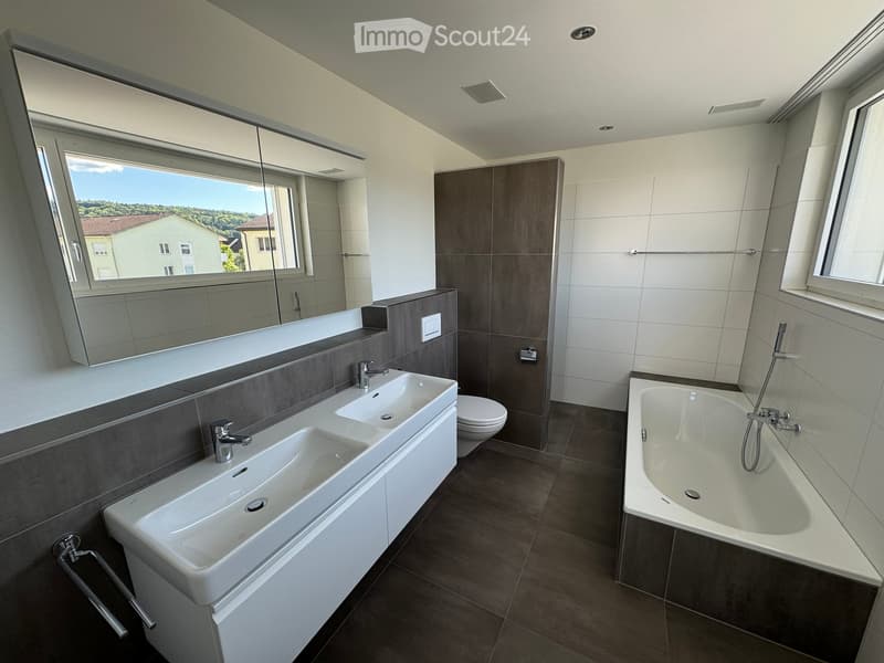 Modern bathroom with double sink, bathtub, toilet, large mirror, and large windows offering a view of the landscape.
