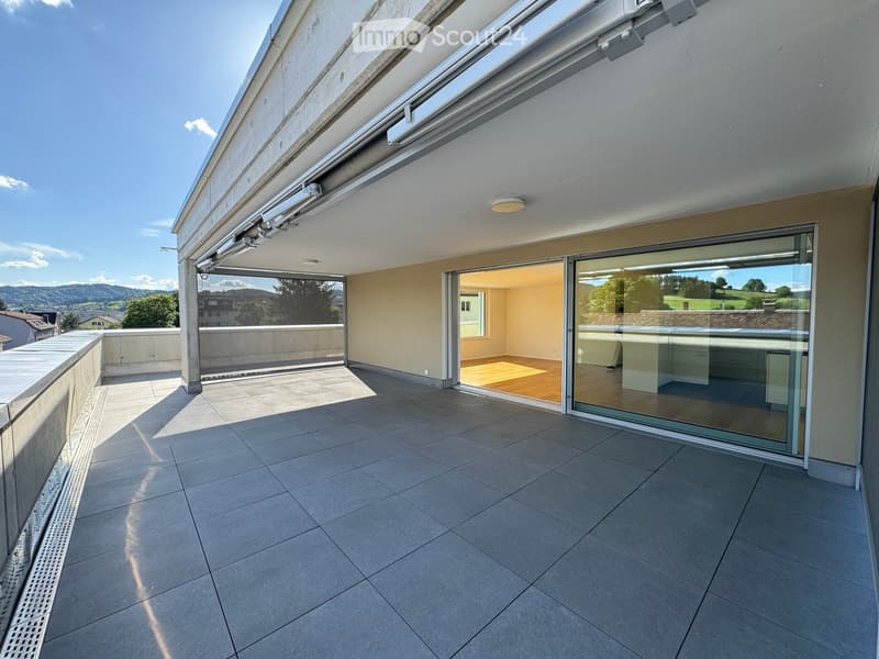 Balcony with tiled floor, large glass sliding doors leading to an interior space, and a view of a green landscape and mountains.