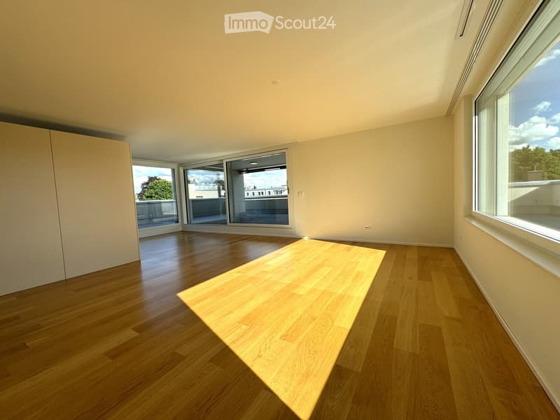 Empty room with wooden flooring, large windows, and sliding glass doors leading to a balcony.