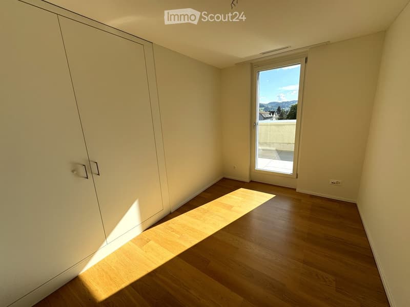 Empty room with light wooden flooring, white walls, and a large sliding glass door leading to a balcony with a scenic mountain view.