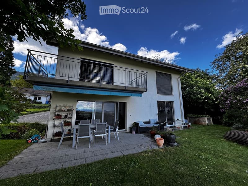Two-story house with a balcony, patio seating area, and garden with lawn and potted plants.