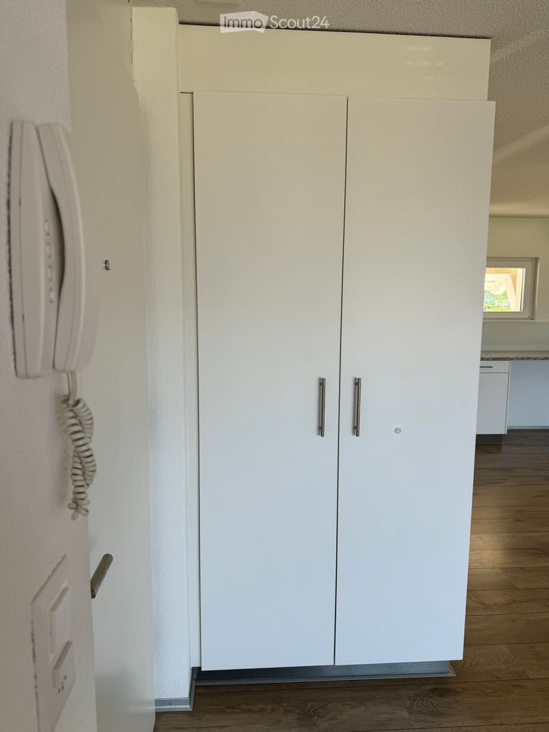 A hallway with white cabinets, a telephone on the wall, and a small window at the end.