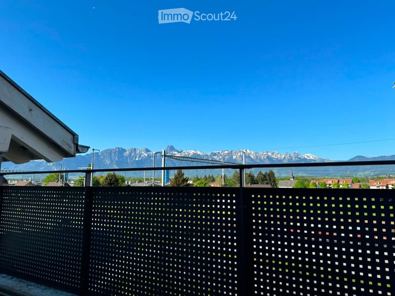 Balcony with a decorative black lattice fence, overlooking a scenic mountain range under a clear blue sky.