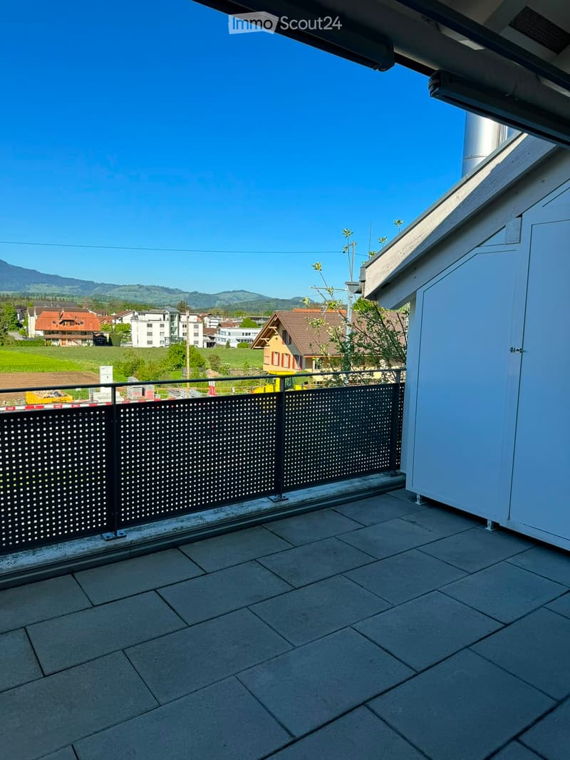 Balcony with a metal railing, tiled floor, and a scenic view of a town and mountains in the background.