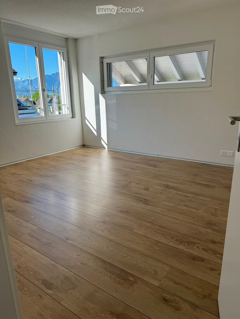 Empty room with wooden flooring and large windows offering a scenic mountain view.