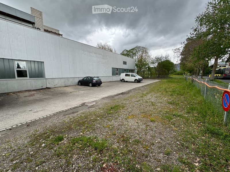 Modern white building with large windows, a fence, and a parking lot with a few cars parked.