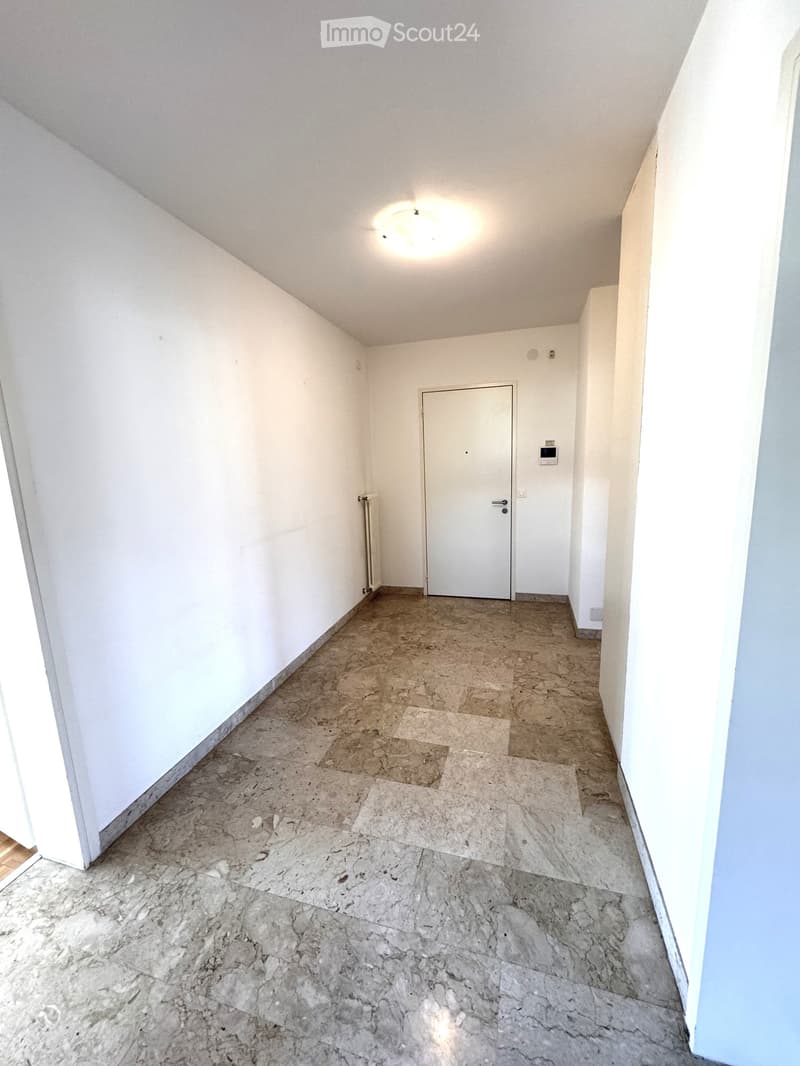 Empty hallway with white walls, marble tiled floor, and a single white door at the end.