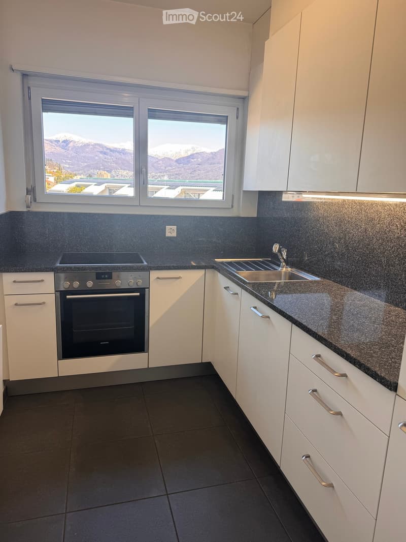 Modern kitchen with white cabinets, dark countertops, stainless steel oven, and sink, overlooking a mountain view.