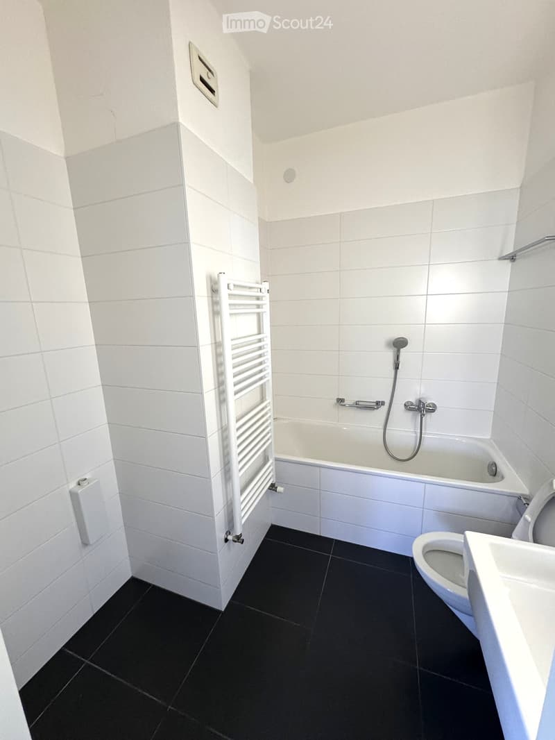 Modern bathroom with white tiles, black floor, bathtub, toilet, sink, and a white radiator.