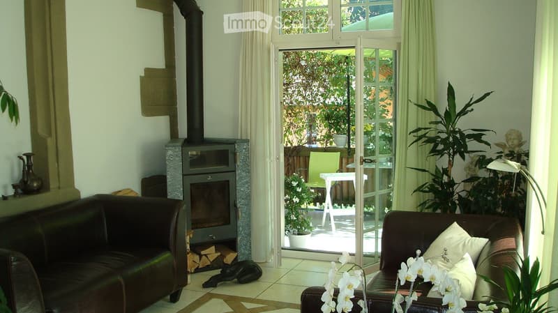 two brown couches, fireplace, white flowers, white curtains, white table, green chair, white table