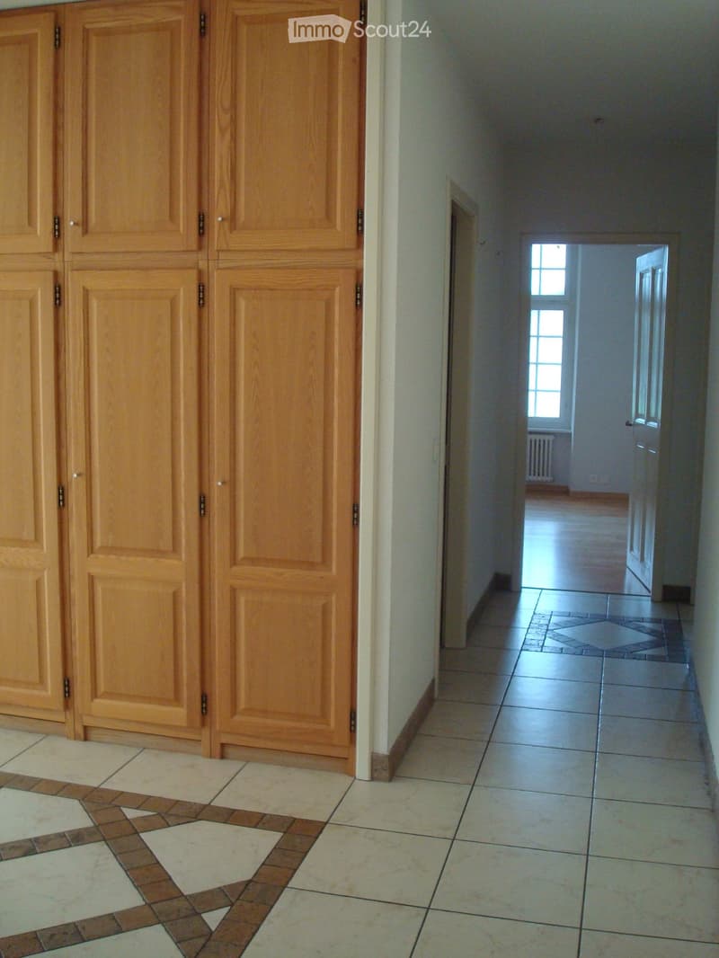 Empty hallway with wooden wardrobes, white tiles, and a wooden floor in the distance