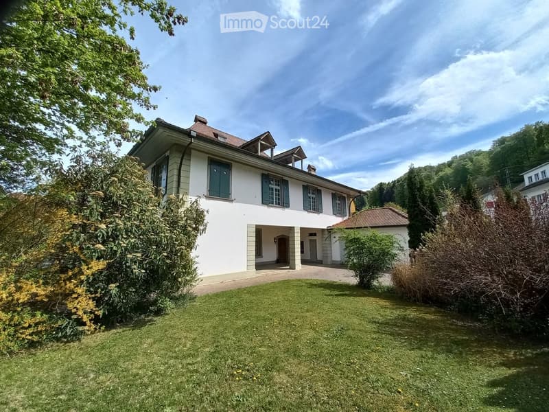 A two-story white house with green shutters, surrounded by a well-maintained lawn and trees.
