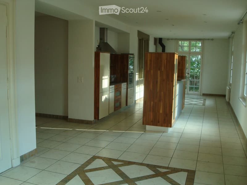 Empty kitchen with white tiles, wooden cabinets, and a glass door leading to a balcony.