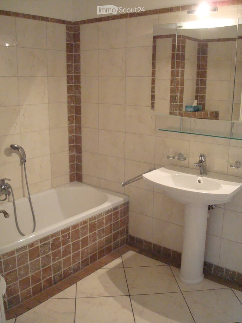 Bathroom with bathtub, sink, mirror, and tiled walls and floor.