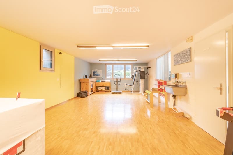 Well-lit room with wooden flooring, featuring a table tennis table, fitness equipment, a sink, and a small cabinet.