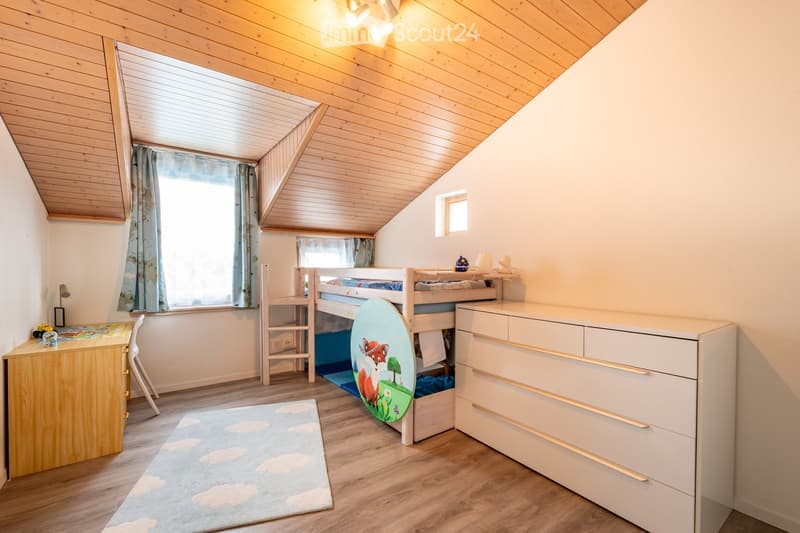 Cozy attic bedroom with wooden slanted ceilings, bunk bed, desk, and storage drawer.