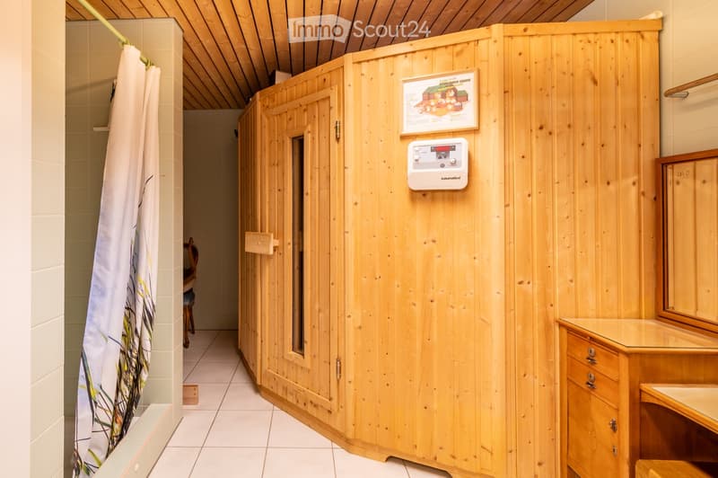 Bathroom with wooden sauna enclosure, shower curtain, mirror, and small wooden stool.