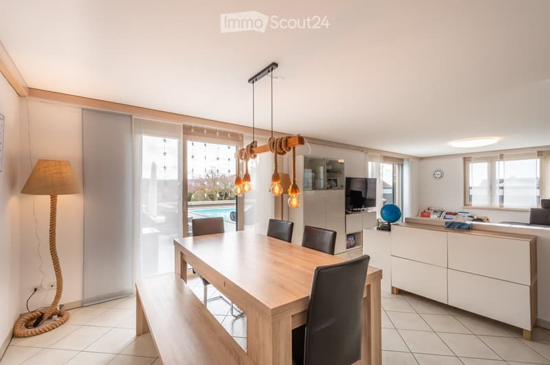 Bright dining area with a wooden table, four black chairs, a tall floor lamp, a television on a cabinet, and a globe on the counter.