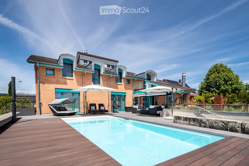Modern house with a spacious outdoor area featuring a swimming pool, lounge chairs, umbrellas, and a wooden deck.