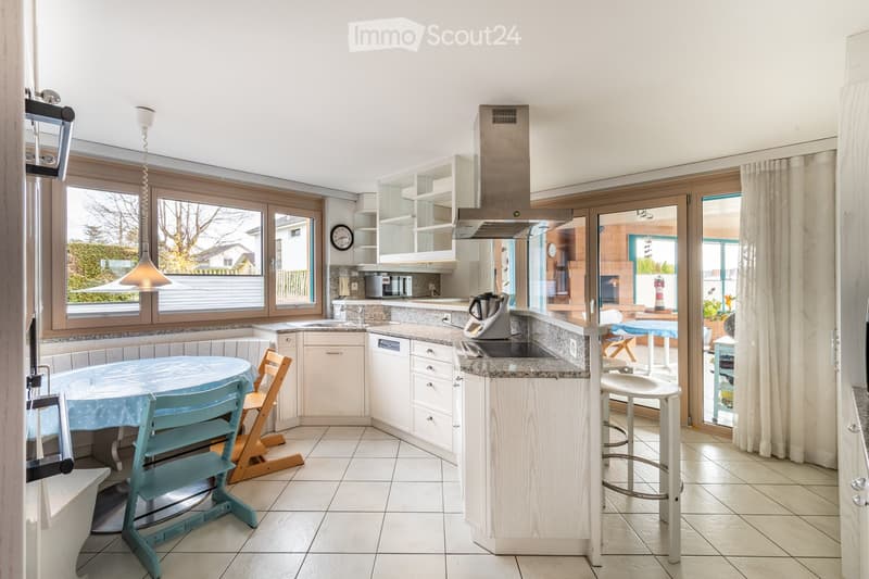 Bright kitchen with white cabinets, granite countertops, and a central island. Features a dining area with a round table and chairs, a microwave, and a view of the outdoor patio through large windows.