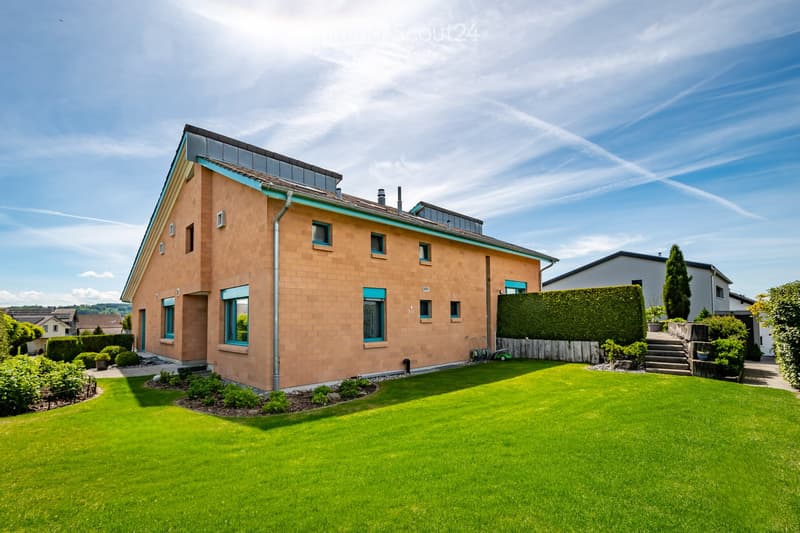 Modern two-story house with a light brown facade, large windows, and a well-maintained lawn in the front yard.