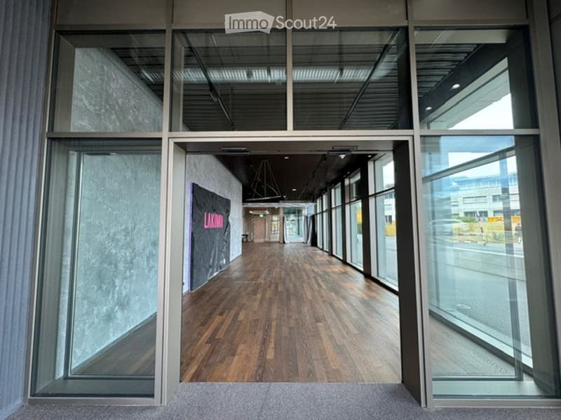 Modern hallway with wooden flooring, large glass windows, and a visible sign on the wall.