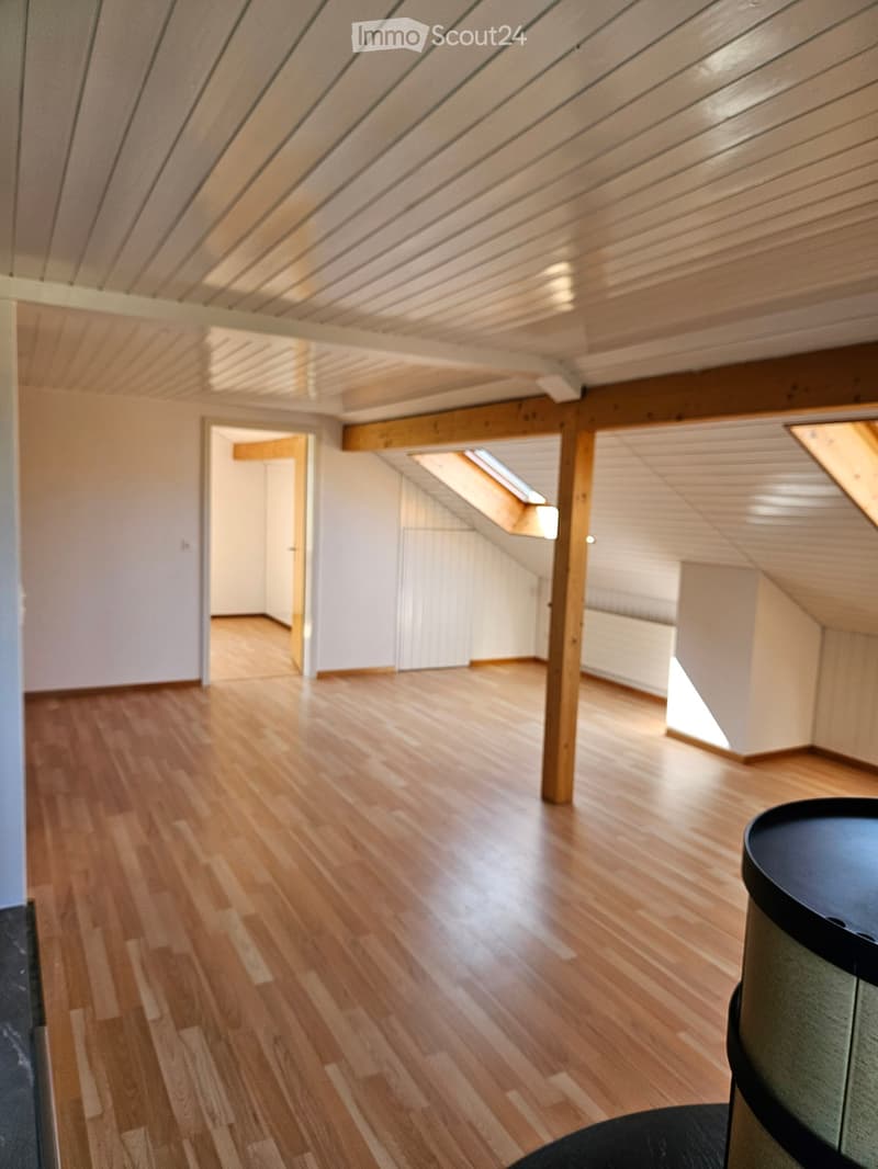 Empty attic space with wooden floors, white walls, exposed wooden beams, and skylights providing natural light.