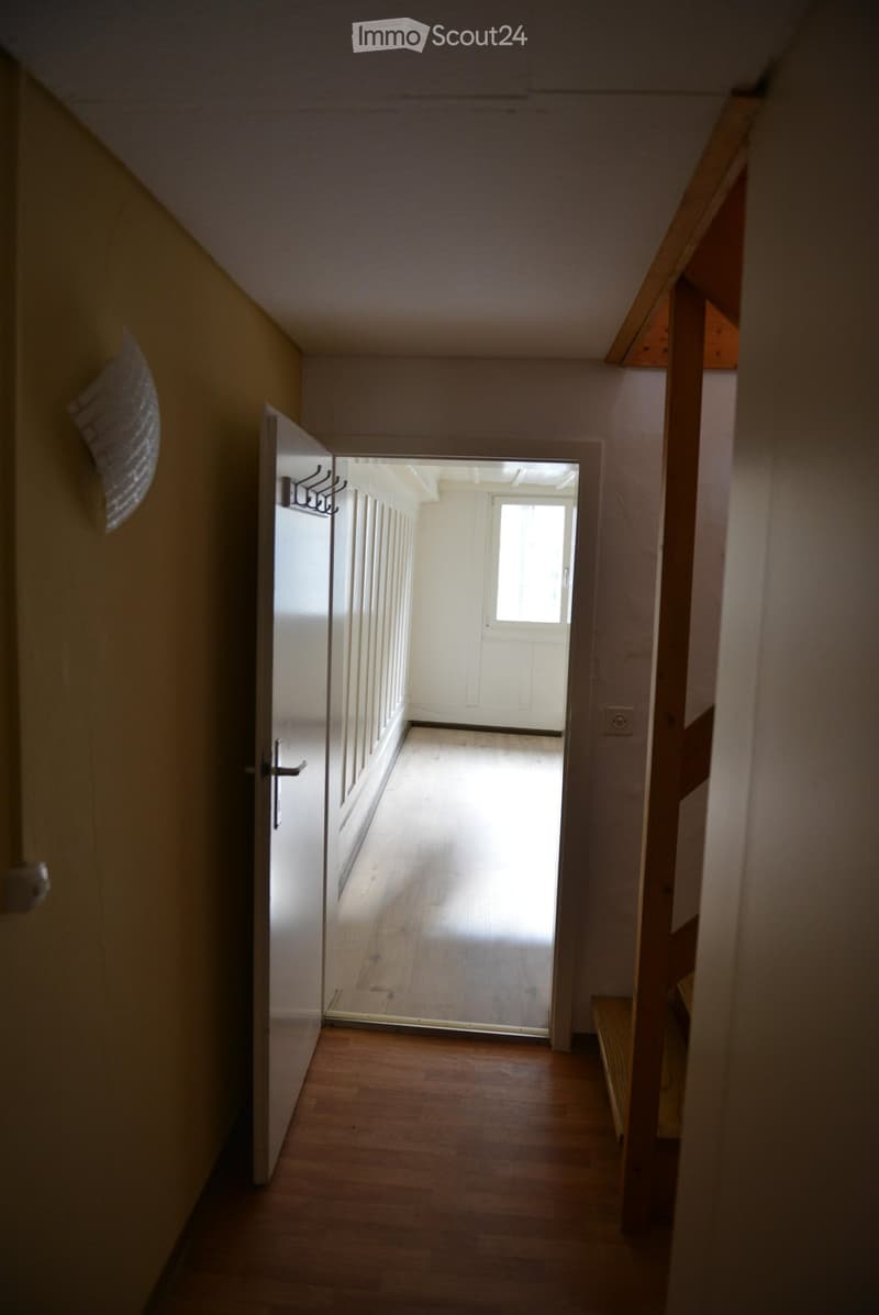 Open hallway with wooden floor, walls, door, and a staircase to upper level