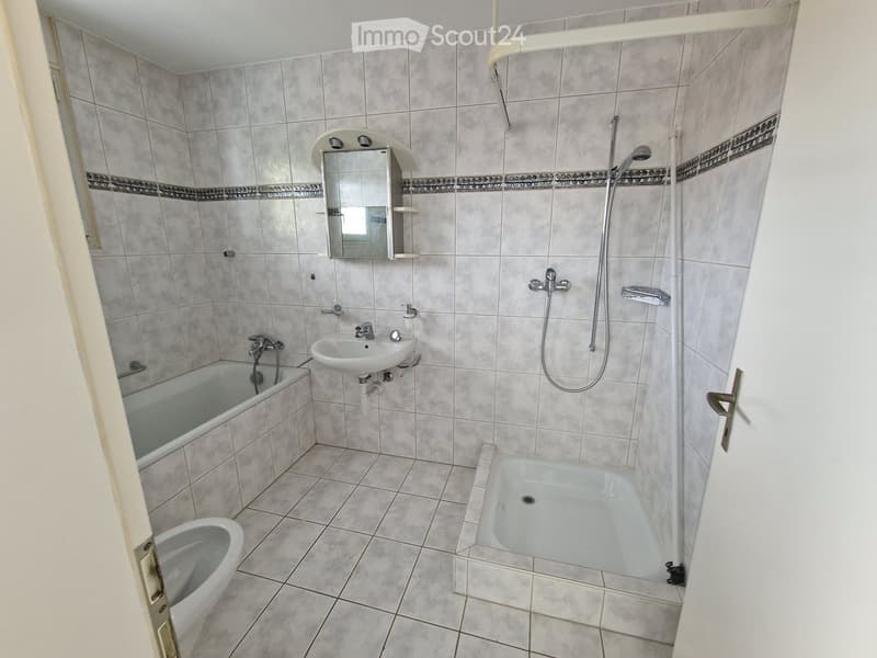 Bathroom with tiled walls and floor, featuring a bathtub, shower, sink, mirror, and toilet.
