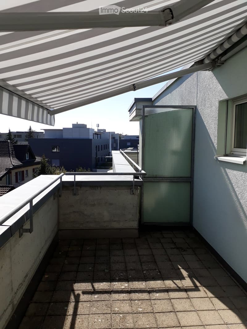Balcony with tiled floor, metal railing, retractable awning, and glass door leading to the interior.