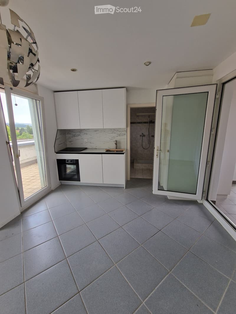 Empty room with tiled floor, white cabinets, and a small shower area visible through an open door. The room has large glass doors leading to a balcony.