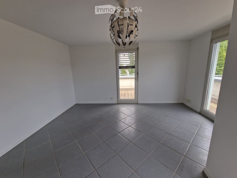 Empty room with light grey tiled floor, white walls, and a modern chandelier hanging from the ceiling. Features a sliding glass door leading to a balcony.