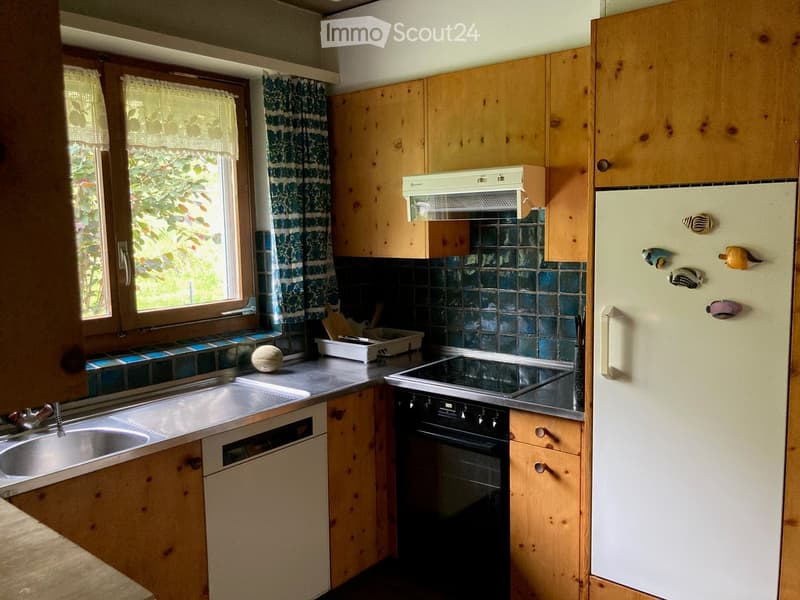 A cozy kitchen with wooden cabinets, a sink, a fridge, an oven, and a ball on the counter. The kitchen features a window with curtains and a tiled backsplash.