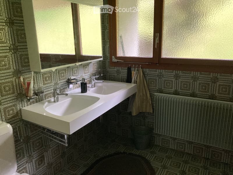 Bathroom with double sink, patterned tiles, mirror, towel, and toiletries.